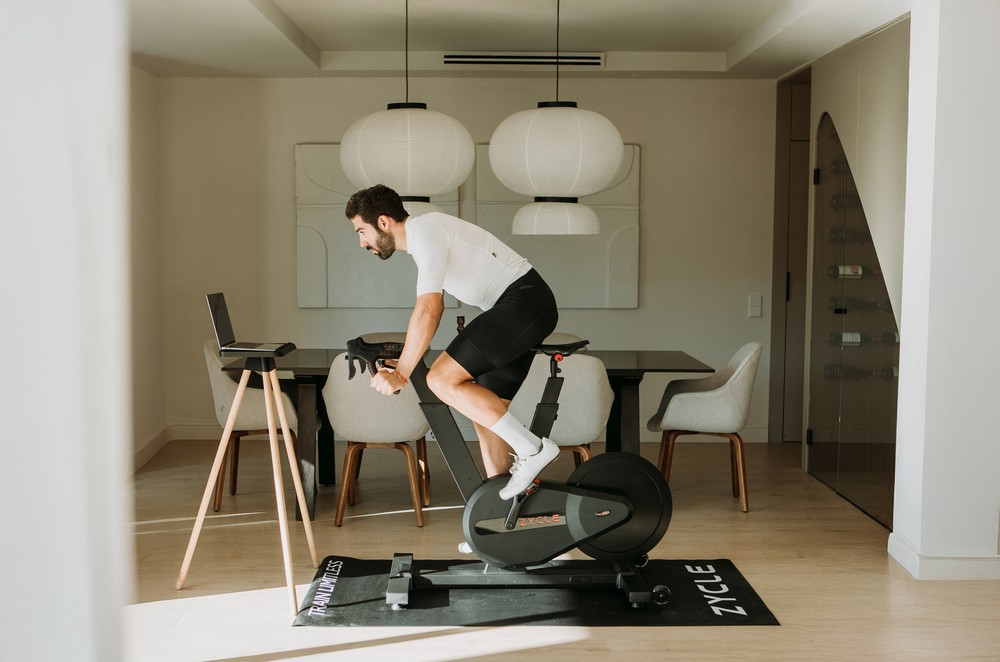 Hombre entrenando en casa en una ZBike Infinity frente a un ordenador portátil.